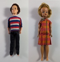 Two vintage dolls are shown against a plain background. The left doll has short, dark curly hair, wearing a striped shirt and dark pants. The right doll has short, light curly hair, wearing an orange plaid dress with a bow.