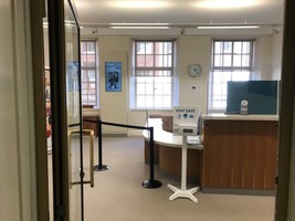 Entrance to Barnsley Archives showing reception desk, sanitisation stand, info screen and clock.