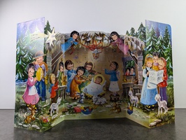 Festive pop-up Christmas scene with children in winter outfits gathered around a nativity display. The backdrop features snowy trees and a starry sky. Animals and presents are visible in the foreground.