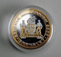 A commemorative coin featuring two figures and a detailed crest in the center. The text around the edge reads "SCHOOLS MILLENNIUM 2000 BARNSLEY." The coin is encased in a clear protective cover.