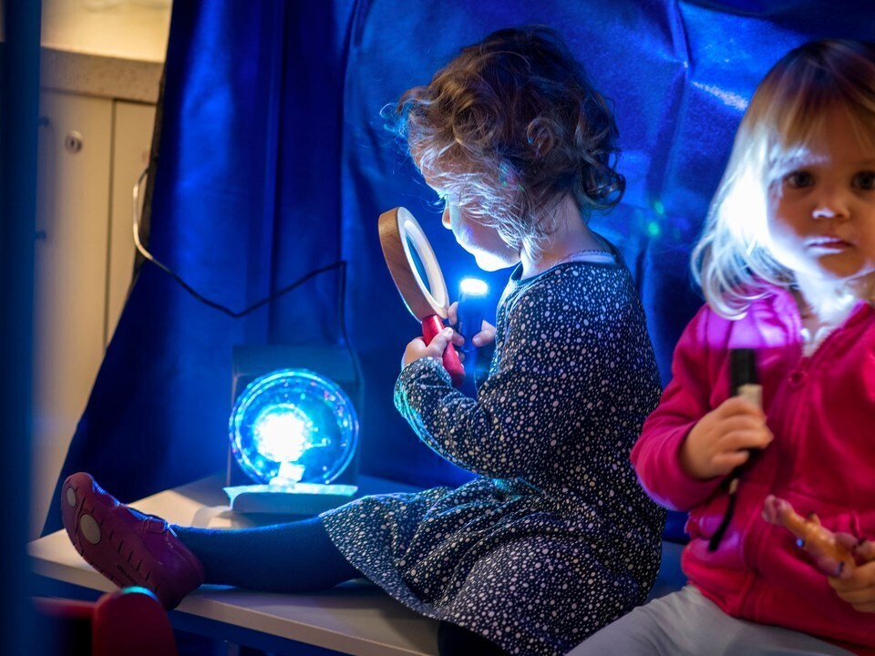 A little girl looking through a magnifying glass at a bright blue light.