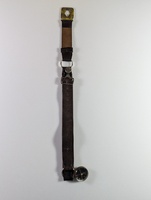 A vintage leather strap with a metal buckle attached at the top and a small round compass at the bottom. The strap is worn and aged, showing signs of use, against a plain light background.