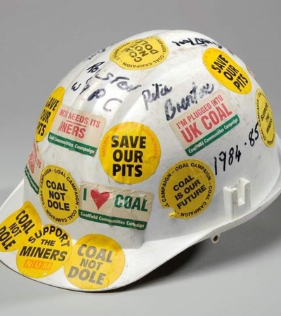 A white coal not dole helmet, it has been decorated with yellow stickers with various slogans