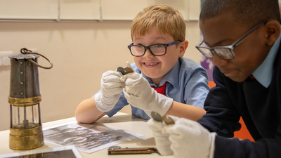 Two children examining coal mining objects including a miners lamp