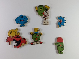 Wooden puzzle pieces featuring cartoon characters, each with different colors and expressions. The characters have distinct shapes and bright colors, arranged randomly on a plain white background.