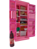 A pink toy fridge with open doors, revealing miniature food items like lard, vegetables, biscuits, cheese, and a can. A small bottle labeled "Cola" stands in front of the fridge.