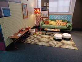 1970s area at Experience Barnsley featuring a green and brown rug, green sofa, small coffee table and two white floor cushions as well as children's toys like a telephone and building blocks.
