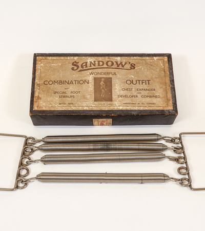 Vintage exercise equipment with a wooden box labeled "Sandow's Wonderful Combination Outfit." Includes metal chest expanders with wooden handles.