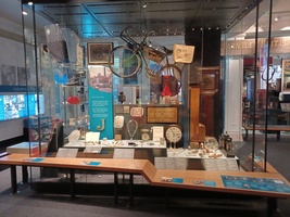 Experience Barnsley Museum main gallery showing a display with a bicycle, small clock and nicknacks such as jewellery and paintings.
