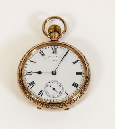 A vintage pocket watch with a round gold case and white face. It features Roman numerals and blue hands, with a small seconds subdial at the six o'clock position. The outer edge is ornately engraved.