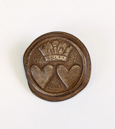 A round, bronze wax seal features two heart shapes side by side, beneath a detailed crown design, on a plain white background.